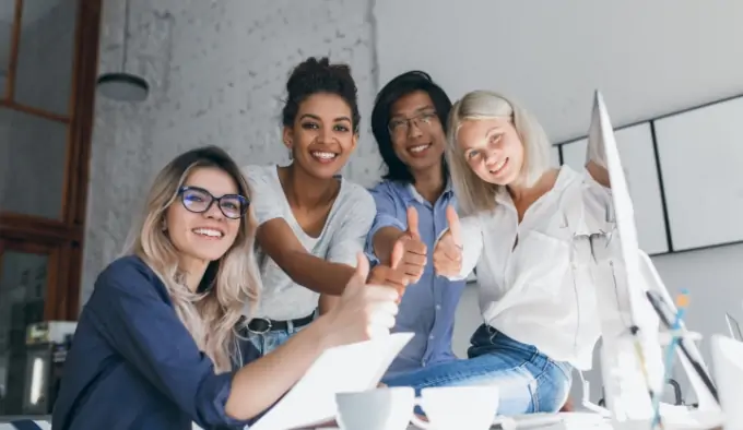 Vier Frauen in Arbeitsatmosphäre zeigen Daumen hoch